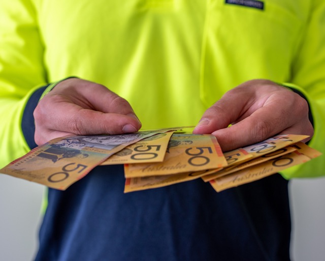 Tradesman receiving wages from work, dressed in a suit and holding fifty dollars note